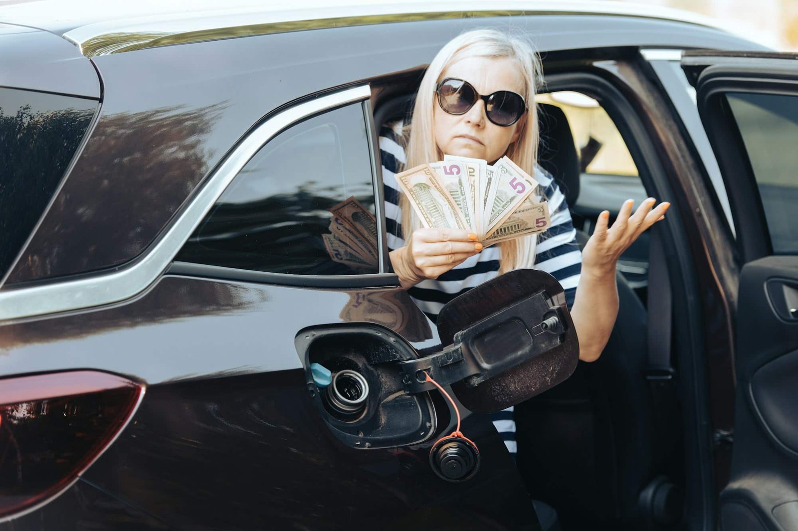 desperate woman hold cash dollar bills in to car with an open tank, concept of rising fuel prices